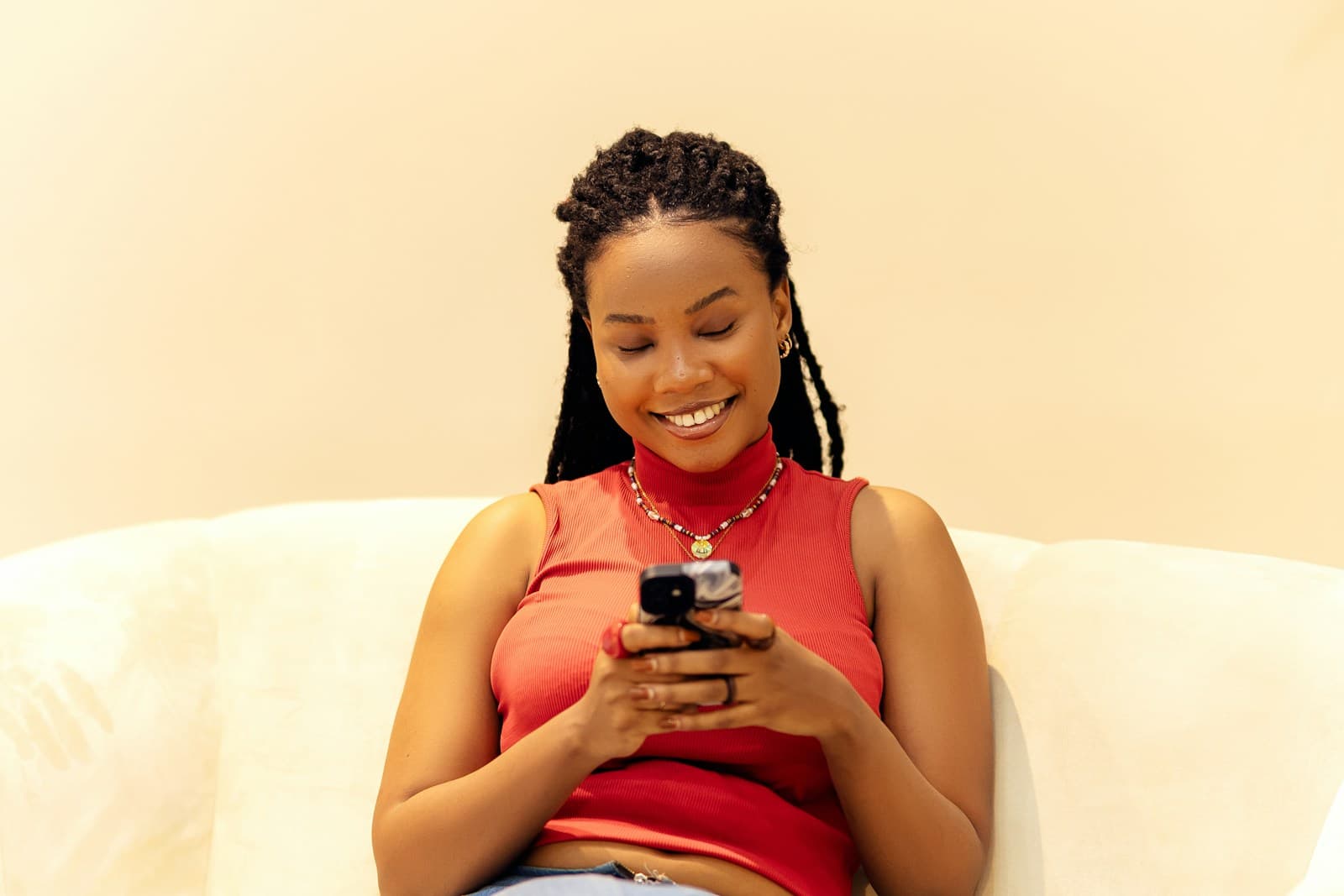 A woman smiling at her phone on the sofa